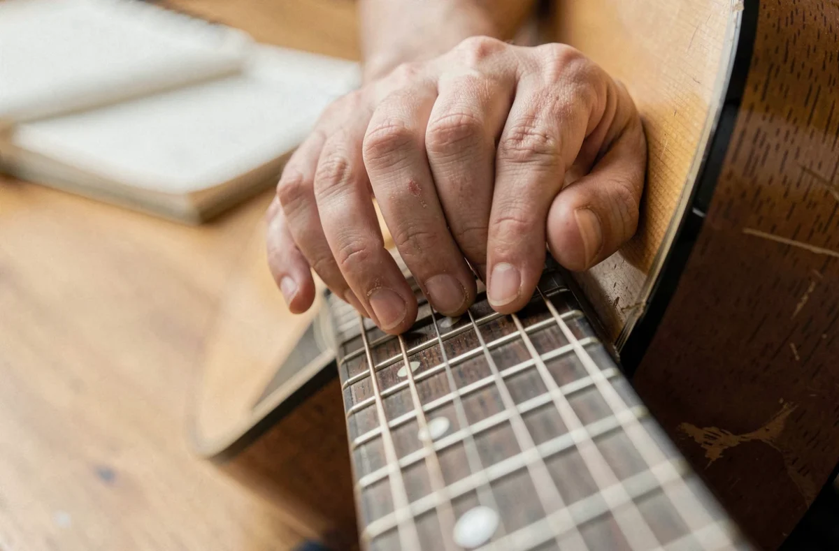 Gros plan des mains d'un guitariste formant un accord simplifié sans barré sur le manche d'une guitare acoustique